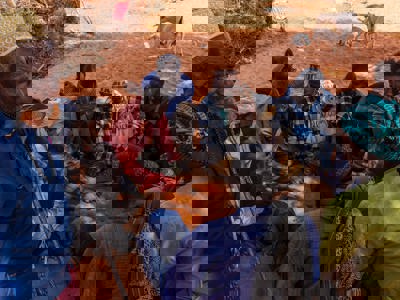 Group of Somaliland men sitting on the orange tinted soil play a game with date stones